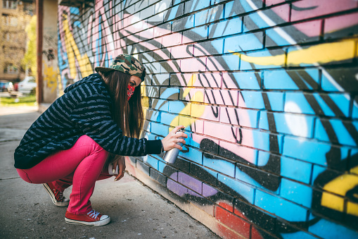 Young woman with bandana is painting graffiti with spray paint