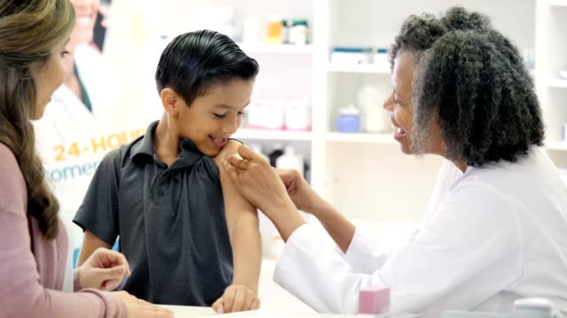 Female pharmacist places bandage on boy's arm after receiving vaccine