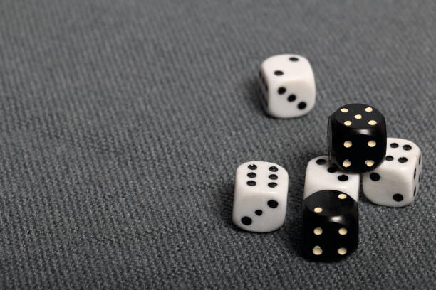 istock White dice with black markings. They lie on a surface covered with a coarse gray cloth. Among them are two black dice with white markings. 1145292298