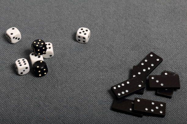 istock White dice with black markings. They lie on a surface covered with a coarse gray cloth. Among them are two black dice with white markings. Next door are dominoes. 1145292300