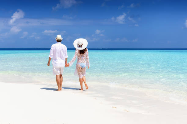 istock Couple in white summer clothes walks along a tropical beach 1145297157