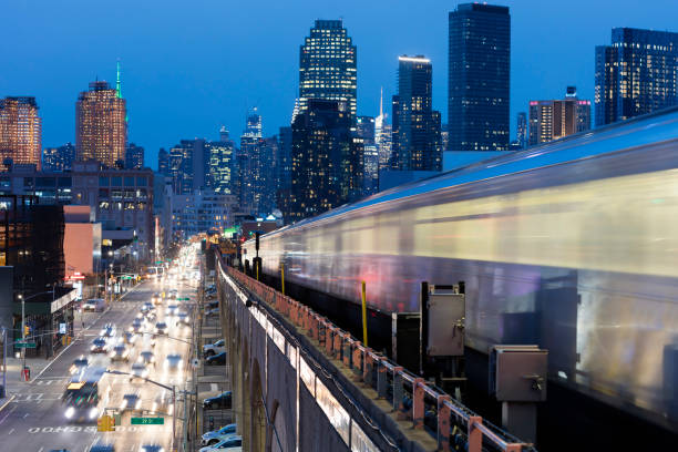 Subway Train Approaching  Elevated Subway Station in Queens, New York Train approaching  elevated subway station in Queens at dusk, New York. Financial buildings and New York skyline are seen in the background, on the left below can be seen a busy street full of cars at rush hour - aerial view, USA. metro area stock pictures, royalty-free photos & images