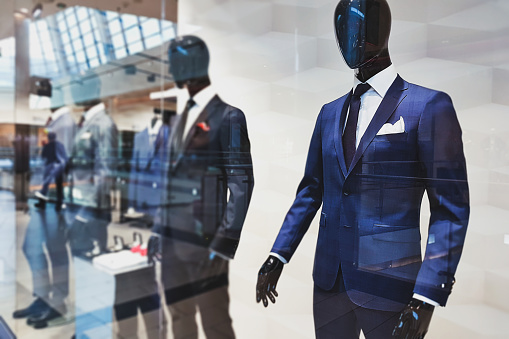 Shopping concept - a storefront with fashionable suits for men presented by mannequins ( selective focus)