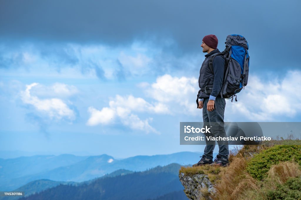 The man with a camping backpack standing on the cliff Above Stock Photo