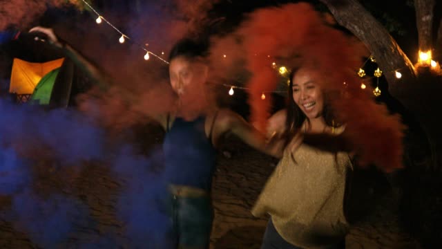 Happy girlfriends women group playing color smoke at beach, Friendship concept with young female friends enjoying time and having genuine fun at camping.