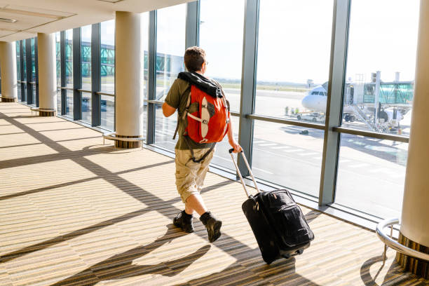 istock Man Wheeling Carry-On Suitcase Through the Airport 1145308936