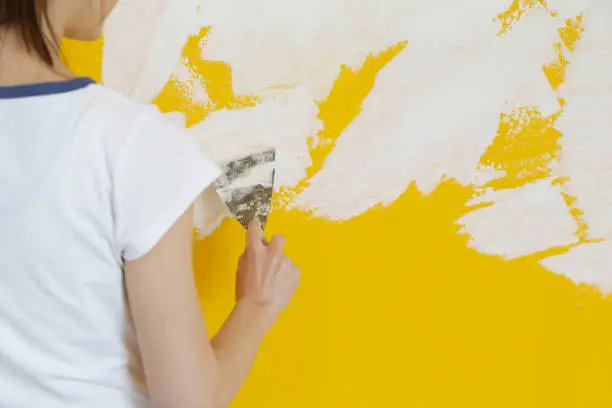 Young woman plastering wall with putty-knife, close up image. Fixing wall surface and preparation for painting, home renovation concept
