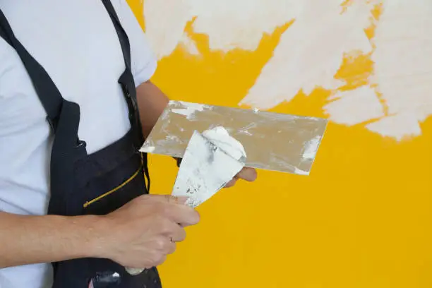 Man plastering wall with putty-knife, close up image. Fixing wall surface and preparation for painting.