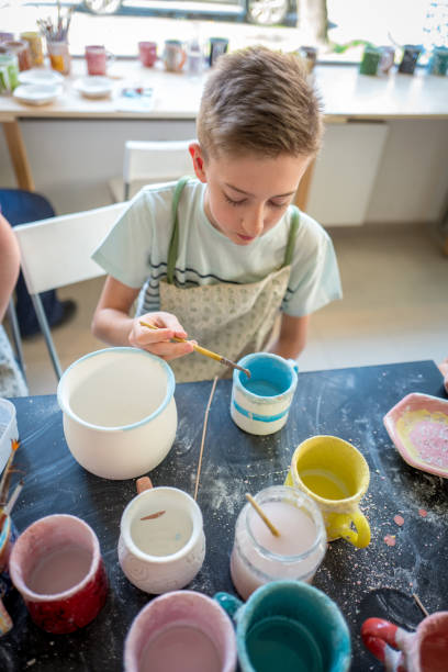 istock Boy concentrating on painting pottery cups 1145327833