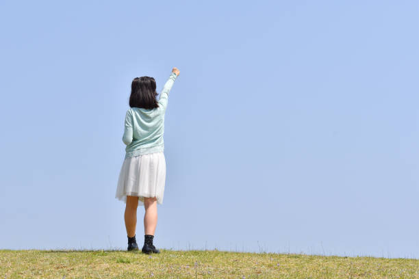 Japanese girl striking a victory pose in the blue sky(Rear view)