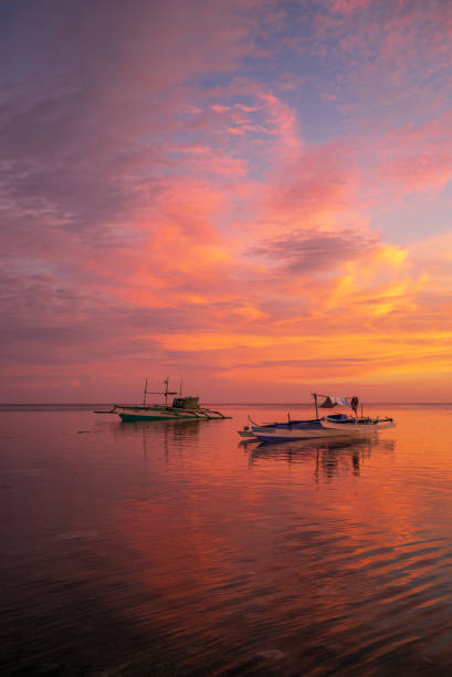 Sunset lighting two boats on Paliton Beach This photo was taken in the Philippines, in the south of the country on the island of Siquijor. We see two boats moored on the beach of Paliton on a pink and blue background in vertical format. siquijor stock pictures, royalty-free photos & images