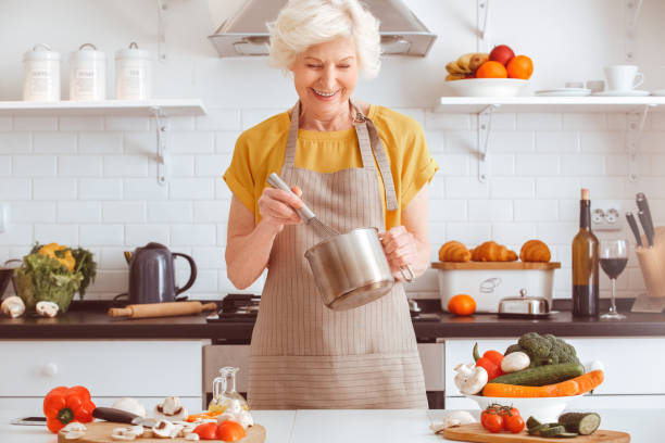 avó considerável que cozinha o jantar do veggie, sorrindo toothy, fazendo o mayo do veggie - grandmother women one person senior adult - fotografias e filmes do acervo