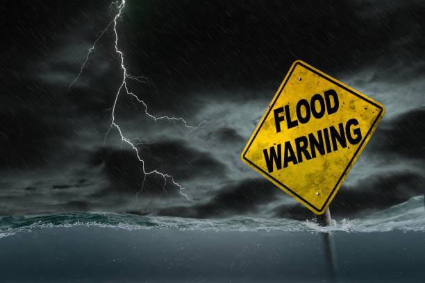 Flood Warning Sign Submerged in Rising Water With Stormy Background Flood Warning sign submerged in rising water against a stormy background with rain and lightning. Dirty and angled sign adds to the drama. flood preparation stock pictures, royalty-free photos & images