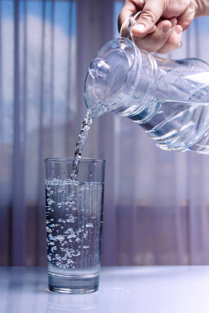 istock Water is poured into a glass from a glass decanter. Light background not uniform background 1145382689