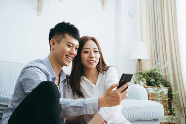 istock Happy young couple using smartphone while relaxing in living room 1145385043