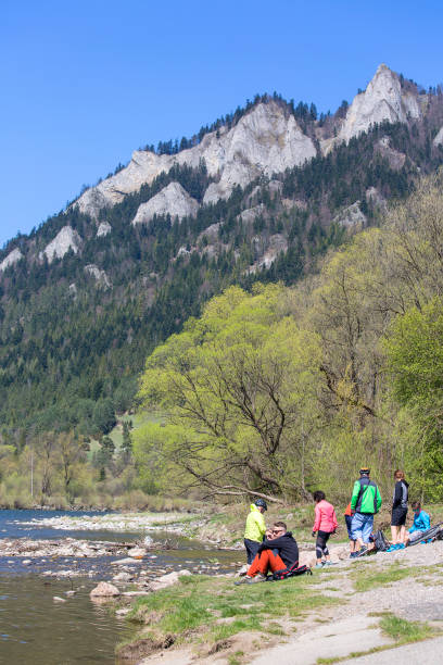 Dunajec River Gorge, Poland - April  20, 2019: View on Three Crowns Massif from the side of the Red Monastery, Pieniny Mountains, resting cyclists on the bank of the river