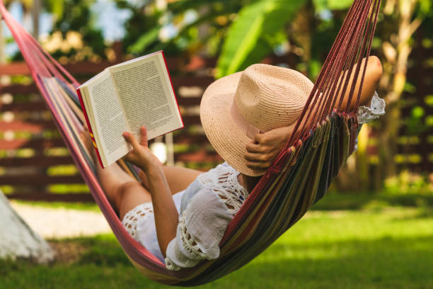 Attractive sexy woman reading book in hammock. Happy beautiful woman in white dress relaxing in hammock. hammock relaxation women front or back yard stock pictures, royalty-free photos & images
