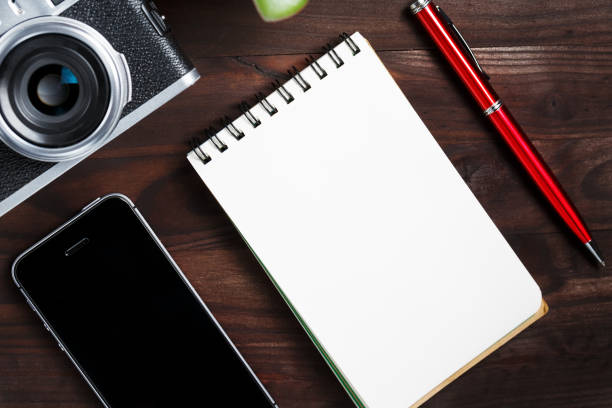 istock Classic camera with blank notepad page and red pen on dark brown wooden table, vintage table with telephone and green flower 1145397730