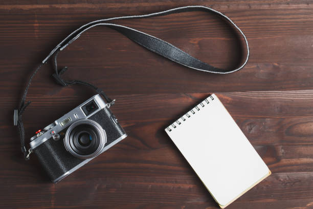 istock Blank notepad page and modern camera in classic style on dark brown wooden table 1145397773