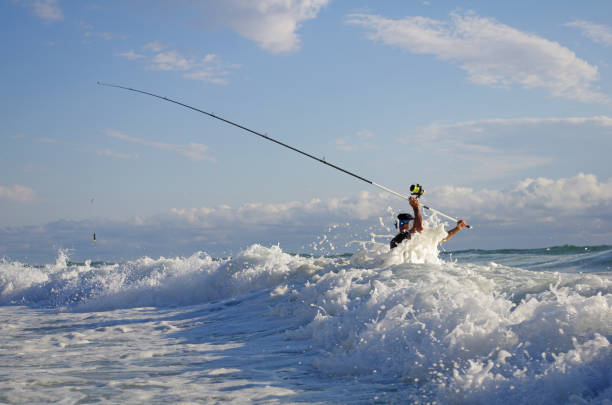 Sea fishing, surf fishing, catch of fish Sea fishing, surf fishing, fisherman into the waves try to cast the line sea fishing stock pictures, royalty-free photos & images
