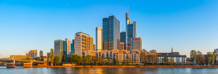 The crowded skyscraper cityscape of Frankfurt’s Bankenviertel financial district illuminated by the  golden sunlight of daybreak above the River Main, Hesse, Germany.