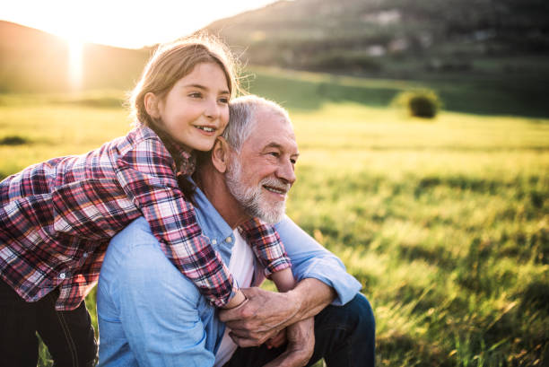 A small girl with grandfather outside in spring nature, relaxing on the grass. A small girl with grandfather outside in spring nature, relaxing on the grass at sunset. granddaughter stock pictures, royalty-free photos & images