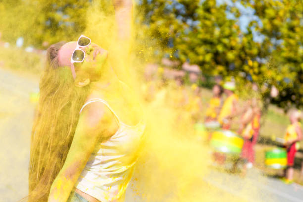 Woman dancing in colors on the holi color festival Woman loving the color festival, laughing and dancing. Colored yellow powder exploding and falling on her. Young candid girl with face paint wearing pink sunglasses and enjoying the event. Drummer Indian musicians in the background. person falling backwards stock pictures, royalty-free photos & images