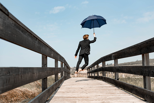 Businessman pulled by umbrella outdoors in non-urban scene.