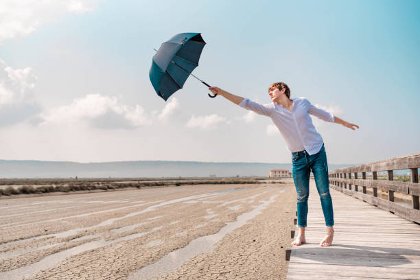 istock Young man holding un opened umbrella on a wooden pier 1145426030