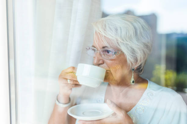 istock Senior woman drinking coffee next to the window 1145430031