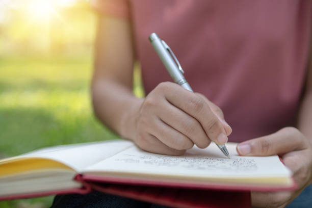 istock poem, poetry and knowledge education concept,  close up sitting writing on notebook in park 1145438840