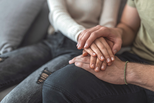 Close up woman and man in love sitting on couch two people holding hands. Symbol sign sincere feelings, compassion, loved one, say sorry. Reliable person, trusted friend, true friendship concept