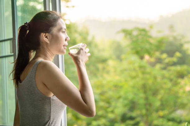 femme asiatique buvant l’eau propre le matin à côté de la fenêtre avec la nature - water women glass healthy eating photos et images de collection