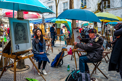 Paris, France - April 15, 2019: A street artist on Montmartre Place du Tertre square in Paris, France is drawing a teenage girl.  The artists sell paintings to tourists.