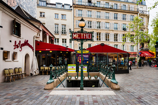 Paris, France - April 16, 2019: An entrance sign for the Metro, underground in Paris, France. In background arre some restaurants.