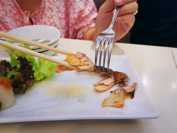 Woman Eating Grilled Salmon using Chopsticks and Fork with Selective Focus