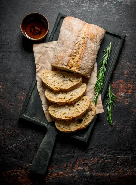 Pieces of ciabatta bread on a cutting Board with rosemary. On dark rustic background