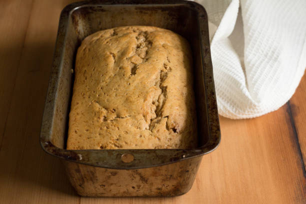istock Banana bread in loaf tin on rustic wooden table with dish towel 1145461358