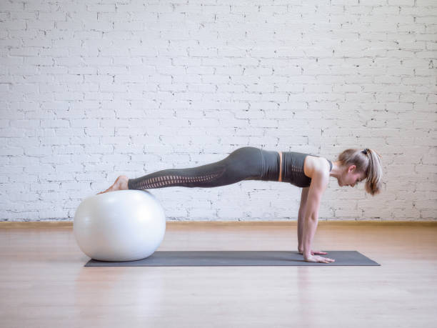 Caucasian woman doing plank position using math and fitness ball, loft background, toned blue Caucasian woman doing plank position using math and fitness ball, loft background, toned blue. Yoga, pilates, fitness, wellness, balance and smart body concept fitness ball stock pictures, royalty-free photos & images