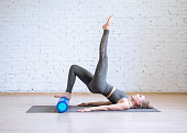 Pilates workout. Woman in grey sports suit doing exercise on math with fitness roller, loft style background, toned light blue