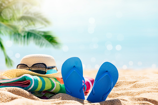 Beach accessories straw hat, flip flops, towel on sunny tropical beach, summer holidays