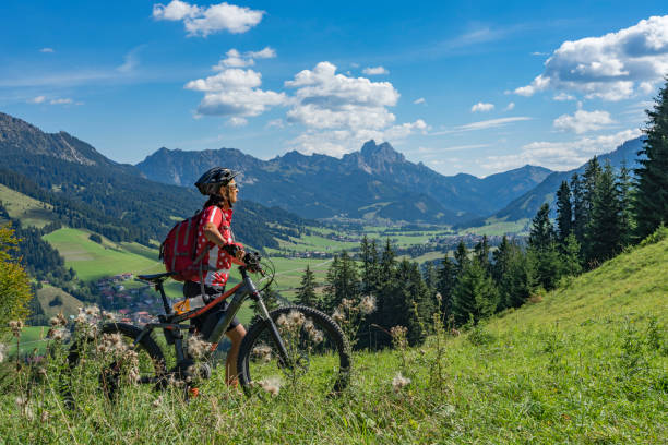 woman with electric mountain bike nice and active senior woman, riding her e-mountainbike in the Tannheim valley, Tirol, Austria with the village of Tannheim and famous summits Gimpel and Rote Flueh tyrol state austria stock pictures, royalty-free photos & images
