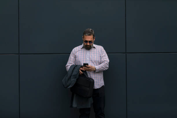 istock Attractive mature businessman wearing suit walking outdoors, using mobile phone 1145483977