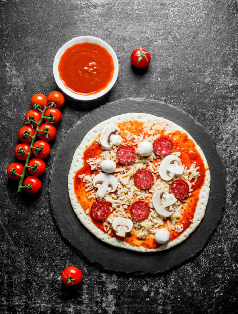 istock Raw pizza with tomato paste, cheese and sausages. 1145485683
