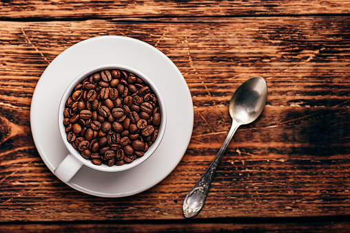 Roasted coffee beans in white cup over rustic wooden surface