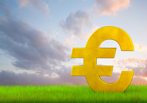 A euro sign in lush green grass on a cloudscape background