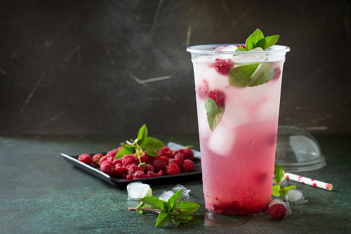 Refreshing summer drink lemon with mint, ice and raspberry with basil, ice. Glasses with cold and healthy beverage on a dark stone background. Copy space.