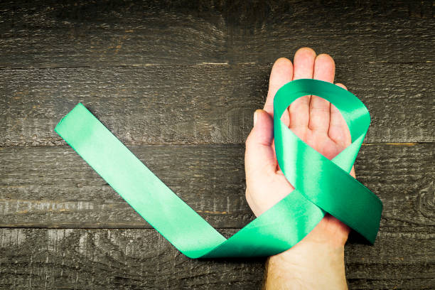 turquoise ribbon on the man's hand, against the background of dark boards - turquoise ribbon alertness doctor imagens e fotografias de stock