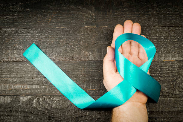 a bright blue ribbon on the man's hand, against the background of dark boards - turquoise ribbon alertness doctor imagens e fotografias de stock