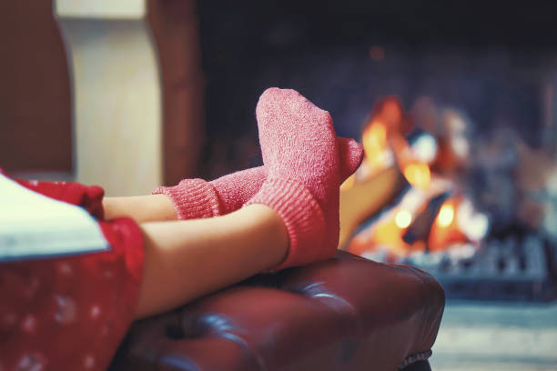 female feet in socks near the fireplace Woman in warm socks resting near fireplace at home with book. Woman feet with socks sitting near fireplace with a warmth background. Toning. heat home interior comfortable human foot stock pictures, royalty-free photos & images